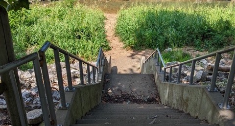 Stairs leading downward to Spring Creek. You can see the creek in the background. The path leading to the creek is very green.